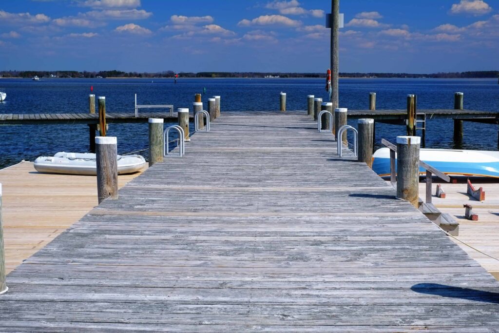 Wooden dock extending into a calm blue lake under a partly cloudy sky, with boats and piers in the background.