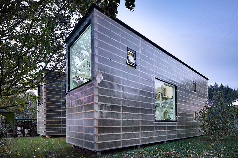 Modern, translucent cladded house with large windows showcasing contemporary design, set amidst lush greenery.