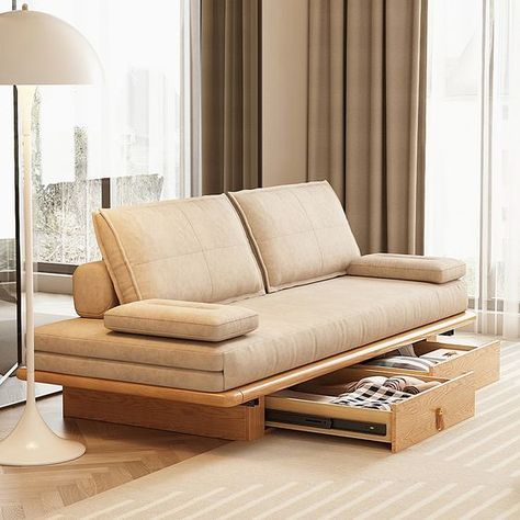 Modern beige sofa bed with built-in storage drawer in a cozy, bright living room with floor-to-ceiling windows.