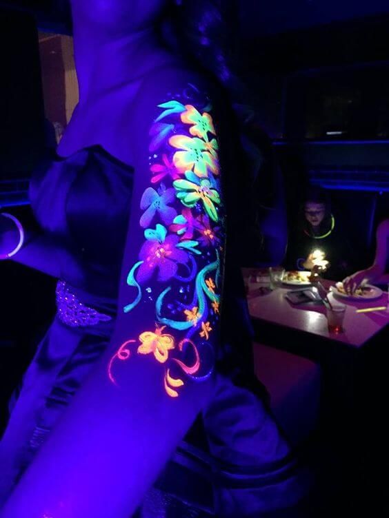 Neon floral body art glowing under blacklight at a party, creating a vibrant and captivating visual effect.