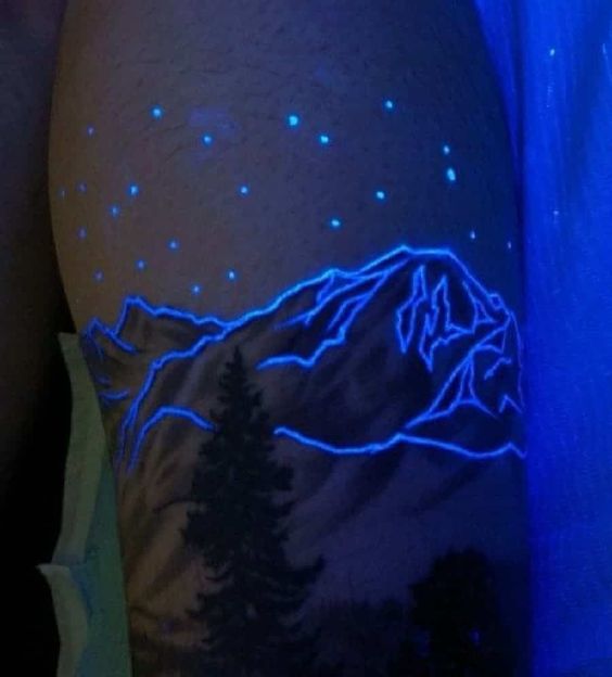 UV tattoo of a mountain landscape with glowing stars on skin, showcasing vibrant blue and purple under UV light.