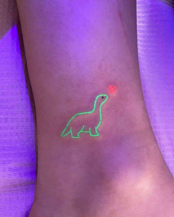 Glow-in-the-dark green dinosaur tattoo with an orange heart on foot under ultraviolet light. Trendy and unique body art.