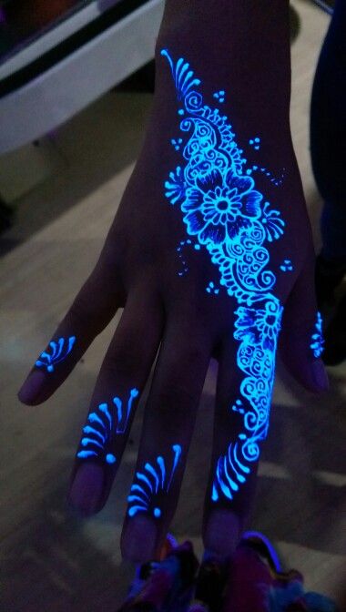 Hand with intricate UV glowing henna design featuring floral patterns, glowing under blacklight.