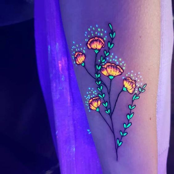 UV tattoo of glowing orange flowers and green leaves on an arm, vividly illuminated under blacklight.