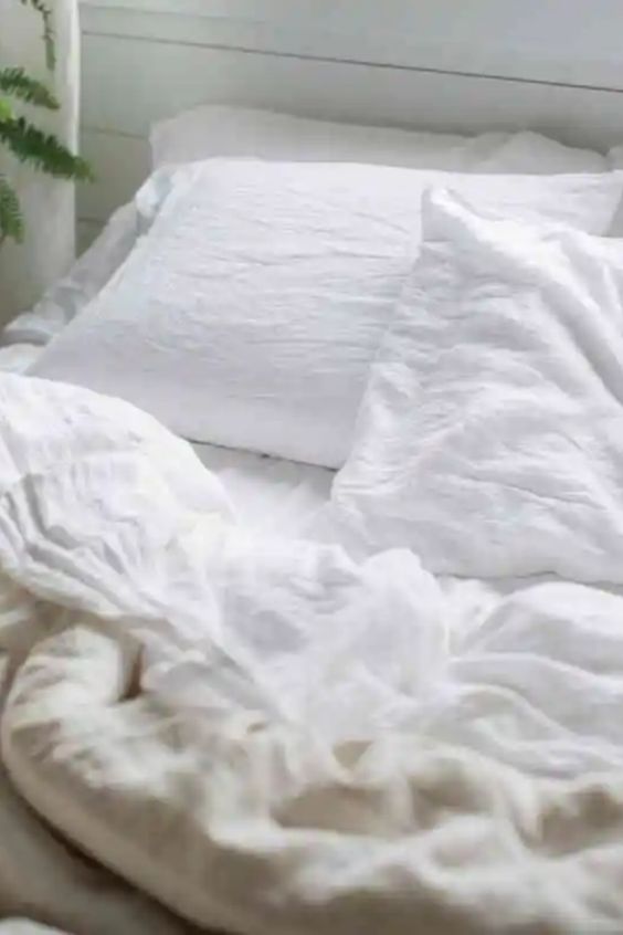 Cozy white bed with rumpled sheets and pillows in a bright, airy room, perfect for relaxation and comfort.