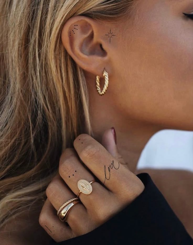 _ 7 Woman's ear with gold hoop earring, hand with gold rings and love script tattoo, close-up detail. | Sky Rye Design Woman's ear with gold hoop earring, hand with gold rings and love script tattoo, close-up detail.