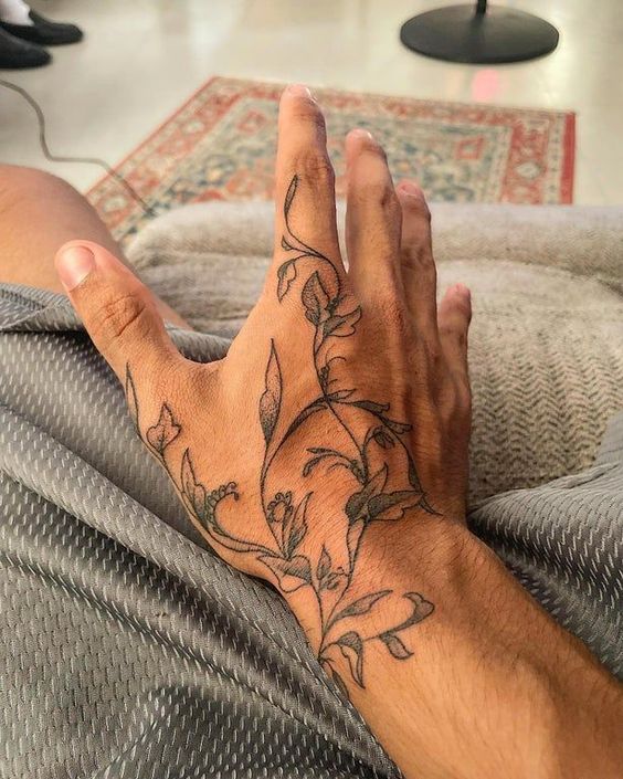 Intricate floral vine tattoo on the back of a person's hand, extending from fingers to wrist, photographed indoors.