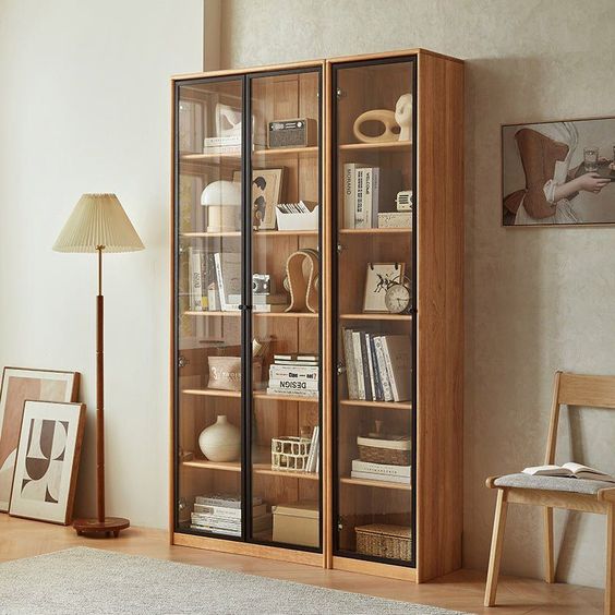 Modern living room with wooden glass-door bookshelf, floor lamp, artwork, and a chair.