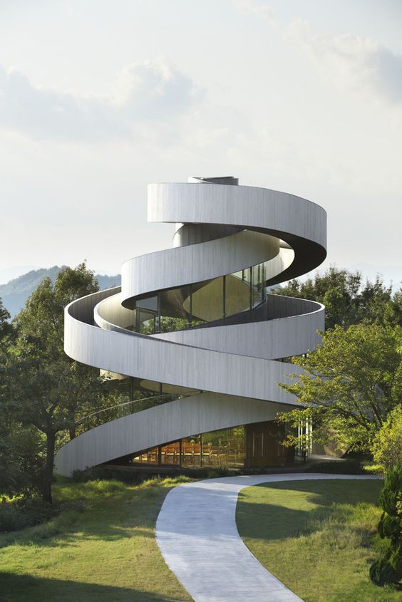 Modern spiral architectural building amidst green landscape with a winding path leading to the entrance.