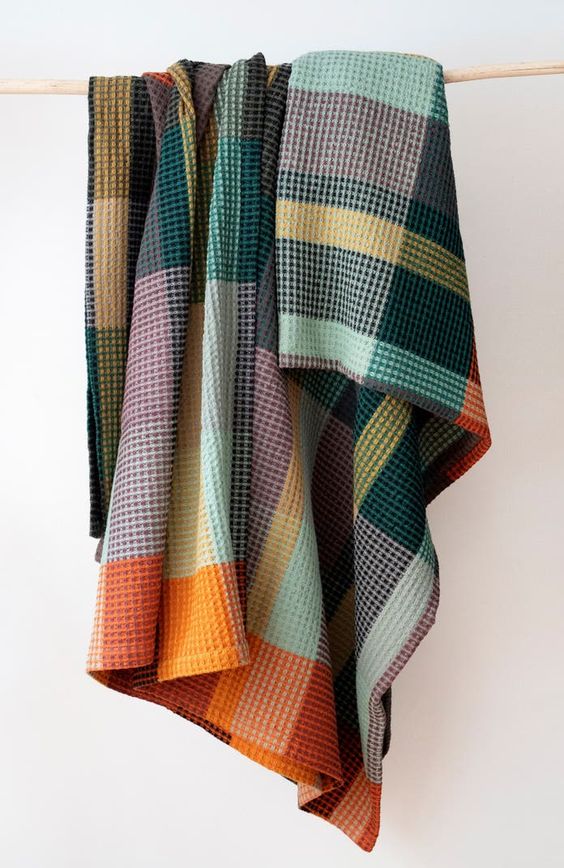 Multi-colored plaid blanket with a honeycomb texture, draped over a wooden rod against a light background.