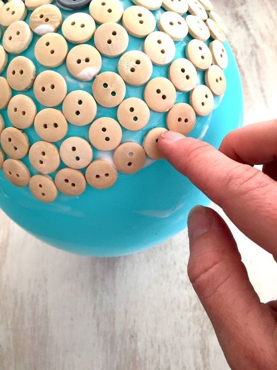 Hand placing wooden buttons on a blue craft ball for a DIY project.