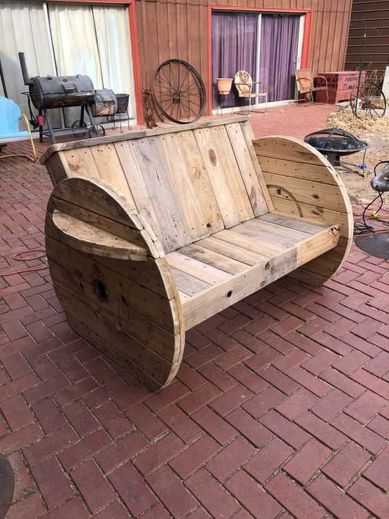 Wooden bench made from repurposed cable spools on a brick patio with rustic outdoor decor in the background.