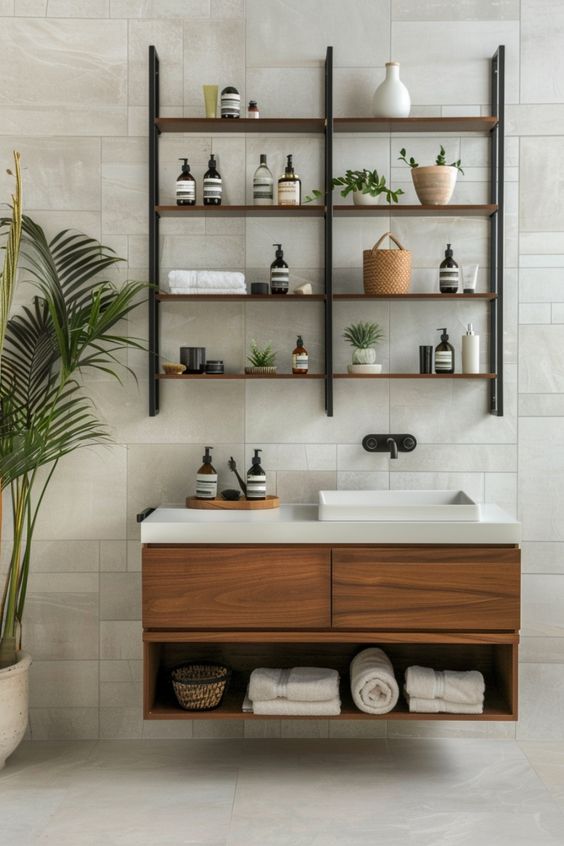 Modern bathroom vanity with wooden floating shelves, stylish decor, and plants, featuring white and wood elements against a tiled wall.