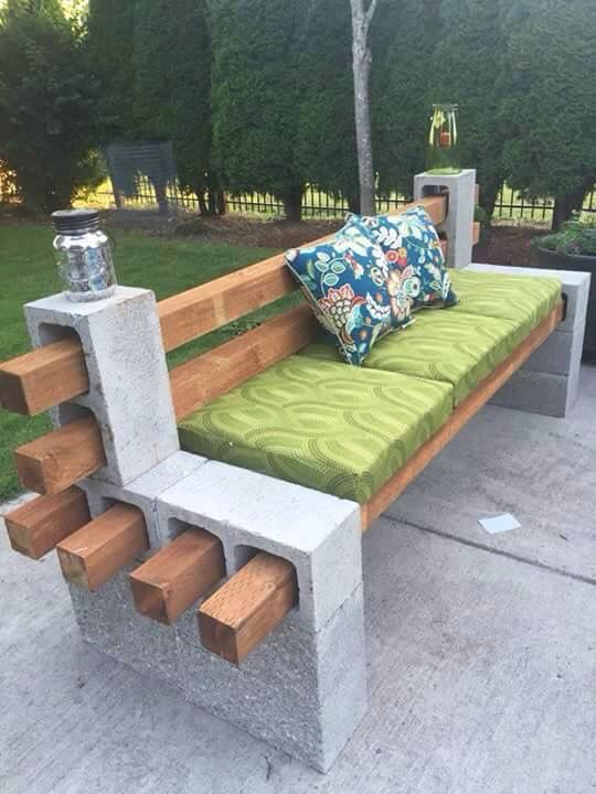 Creative DIY garden bench made from cinder blocks and wooden beams with green cushions and colorful pillows on a patio.