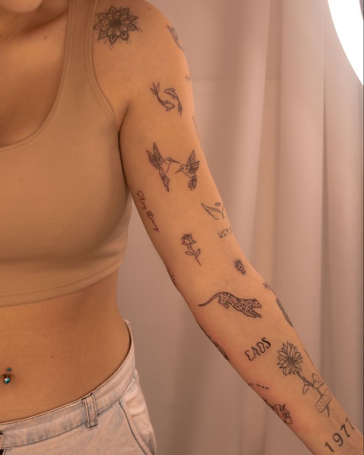Classy Arm Tattoos for Women 1 Person with floral and animal tattoos on arm, showcasing creative body art in soft lighting. Wearing a beige crop top and light jeans. | Sky Rye Design Person with floral and animal tattoos on arm, showcasing creative body art in soft lighting. Wearing a beige crop top and light jeans.