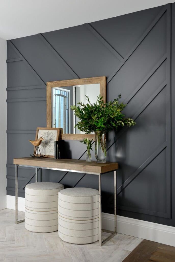 Modern entryway design with gray accent wall, wooden console table, decorative mirror, plants, and round stools.