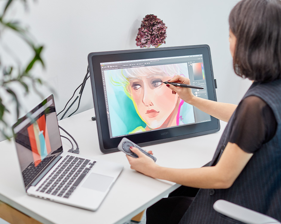 Digital artist drawing portrait on a graphics tablet connected to a laptop, showcasing creativity and design skills.