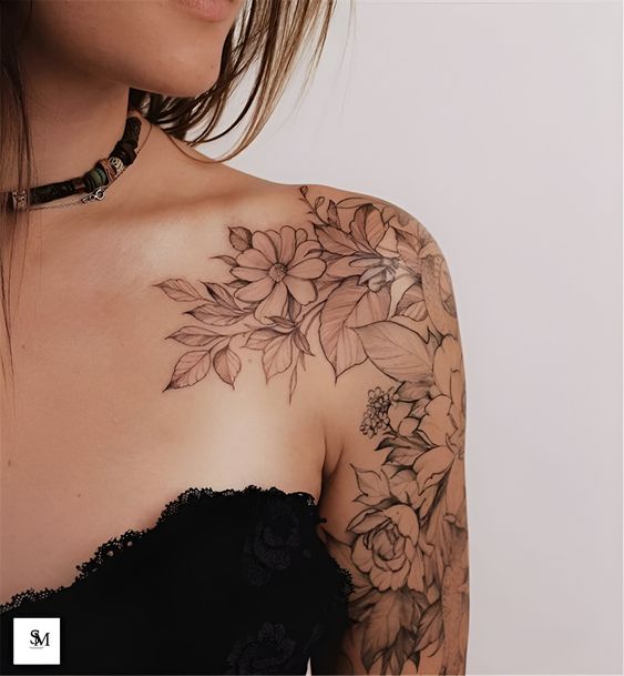 Close-up of woman with detailed floral tattoo on shoulder and arm, wearing black lace top and necklace.