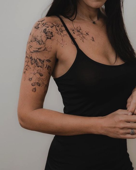 Woman wearing a black tank top, showcasing a detailed floral tattoo on her shoulder and upper arm.