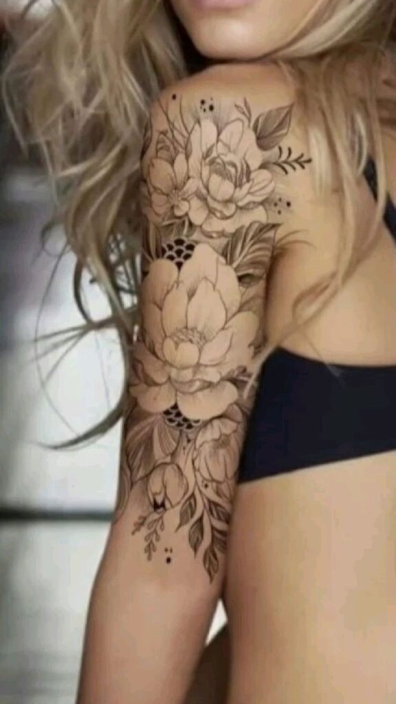 Woman with intricate floral tattoo design on her upper arm, showcasing beautiful flowers and leaves in black ink.