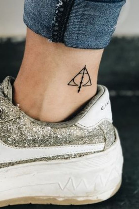 Ankle tattoo of the Deathly Hallows symbol from Harry Potter, paired with glittery sneakers and blue jeans.