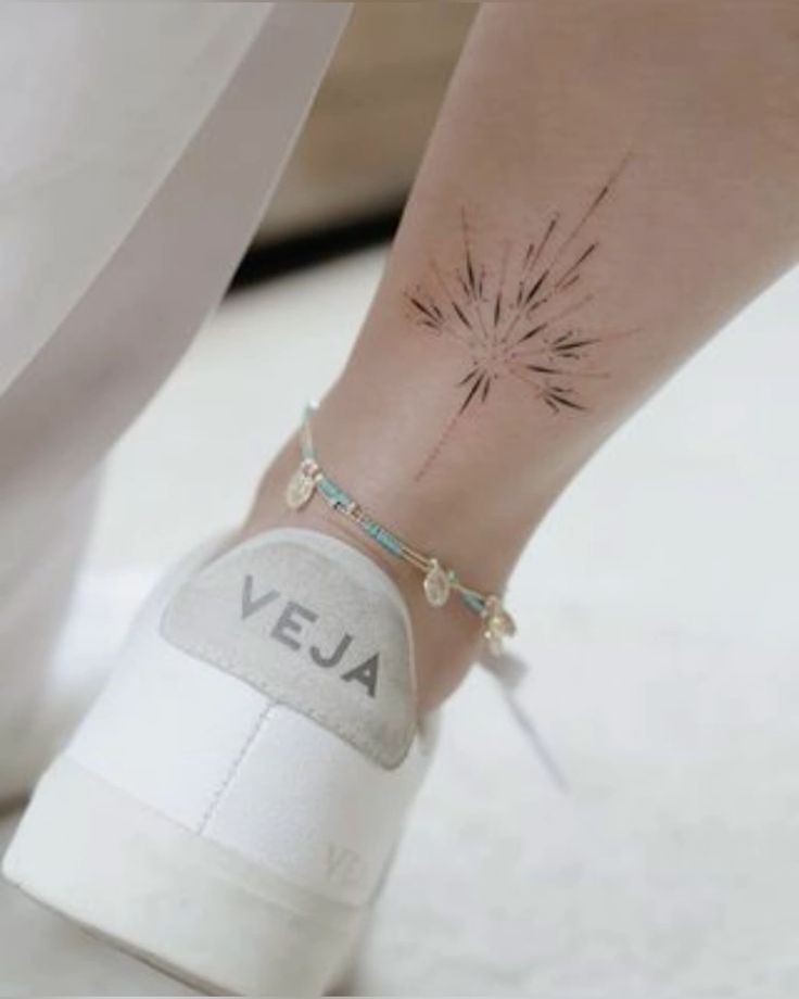 Close-up of an ankle tattoo with a geometric design, wearing a blue anklet and white Veja sneaker.