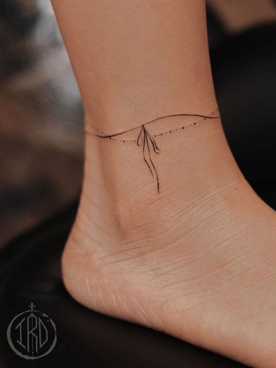 Minimalist ankle tattoo with a dainty design resembling an anklet with flowing lines and dots.