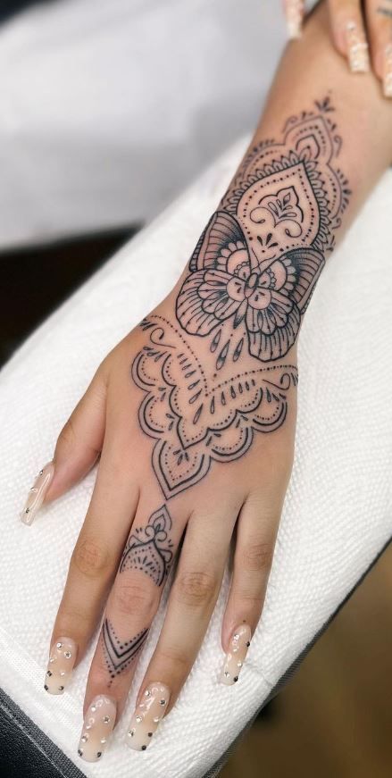 Hand adorned with intricately detailed black henna tattoo, showcasing a butterfly and floral patterns along the fingers.