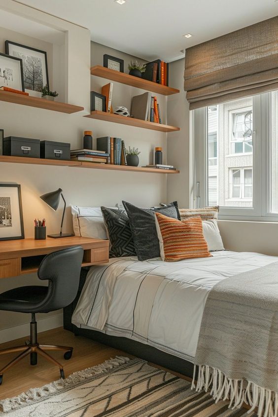 Cozy modern bedroom with a desk and wall shelves, featuring neutral decor, multiple pillows on the bed, and a large window.