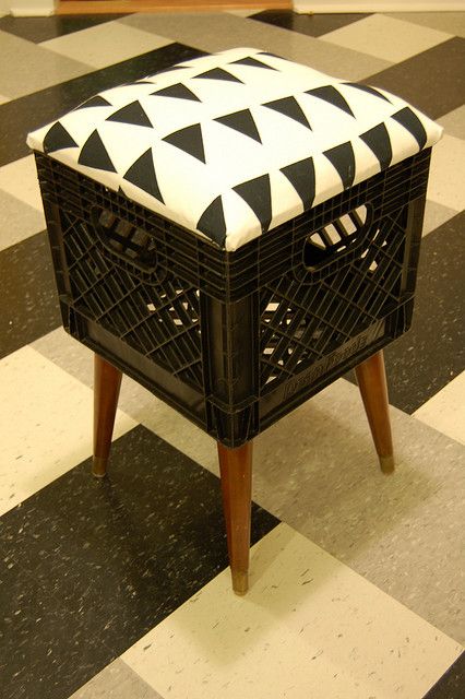 DIY stool featuring a black crate base and a cushion top with black triangles on white, placed on a checkered floor.