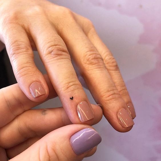 Close-up of hands showcasing delicate minimalist heart tattoo and nude manicured nails. Elegant and simple nail art design.