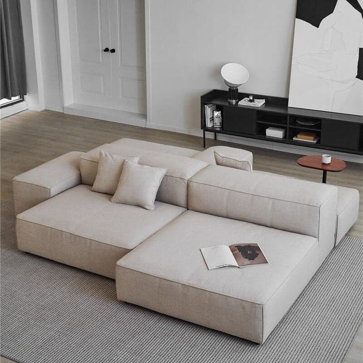 Modern minimalist living room with beige sectional sofa, abstract art, and a sleek black console table.