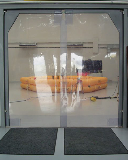 Plastic industrial door with a view of an orange inflatable raft inside a sterile-looking room with equipment on the floor.