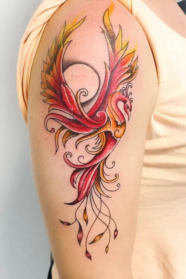 Colorful phoenix tattoo with vibrant wings and flowing tail feathers on a person's upper arm.