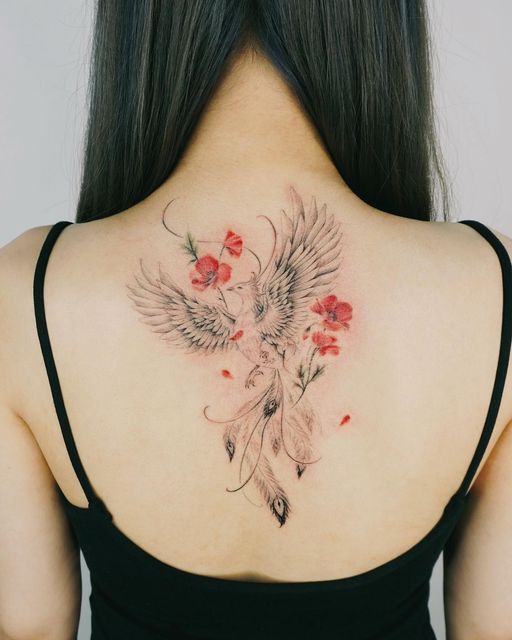 Woman with long hair showcasing an intricate back tattoo of a phoenix with red and pink flowers, wearing a black strappy top.