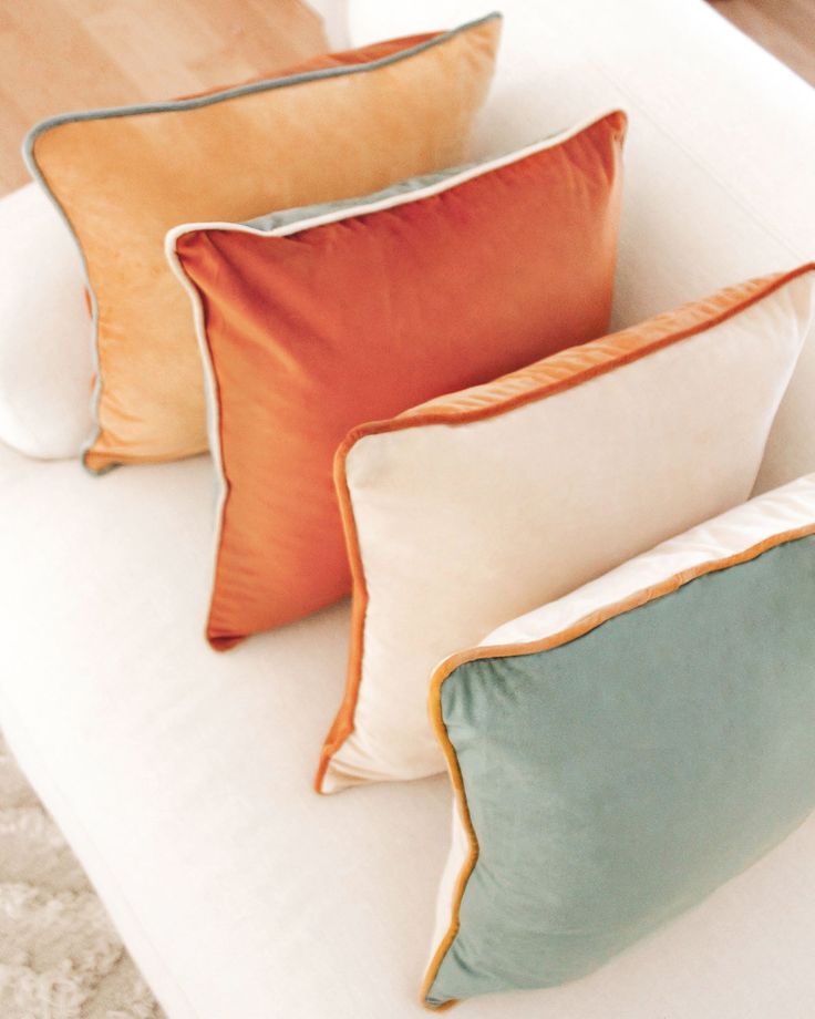 Colorful velvet throw pillows in shades of orange, beige, and teal arranged neatly on a white sofa for a cozy and stylish decor.