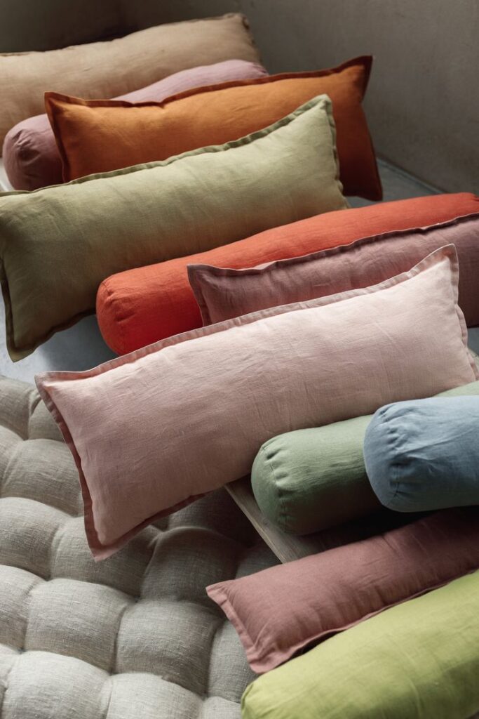 Assorted colorful linen bolster pillows arranged on a cushioned surface for cozy home decor styling.