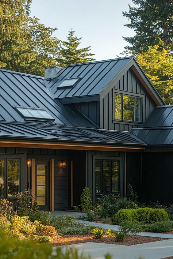 Modern black farmhouse with sleek metal roof, large windows, and beautiful landscaping in a forest setting.