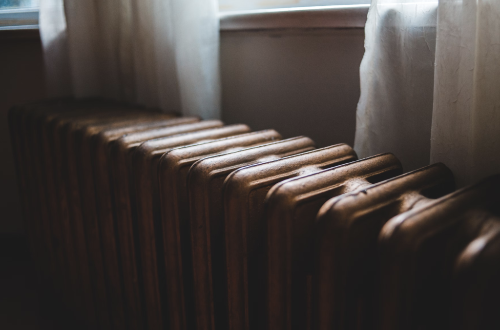 Vintage metal radiator in a cozy room near a window with sheer curtains, radiating warmth and nostalgia.