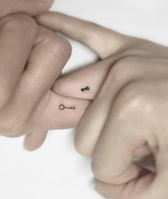 Close-up of two fingers with matching key and keyhole tattoos, symbolizing connection and love.