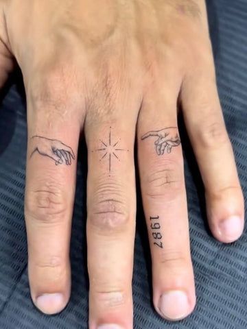 Hand with minimalist finger tattoos including a star in the center and 1987 on the ring finger against a dark background.