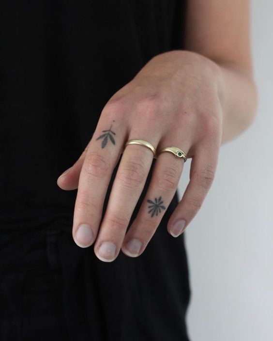 Close-up of fingers with minimalist tattoos and gold rings, showcasing simple hand jewelry and body art design.