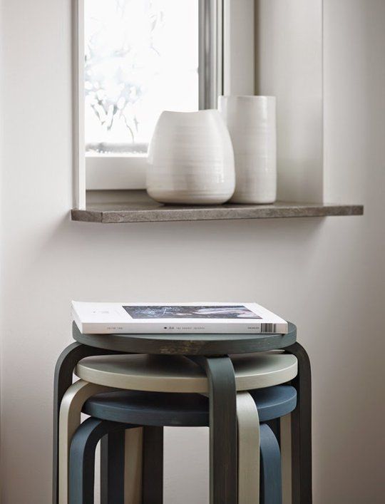 Stacked modern stools beside window shelf with white ceramic vases and a book, minimalistic home decor setup.