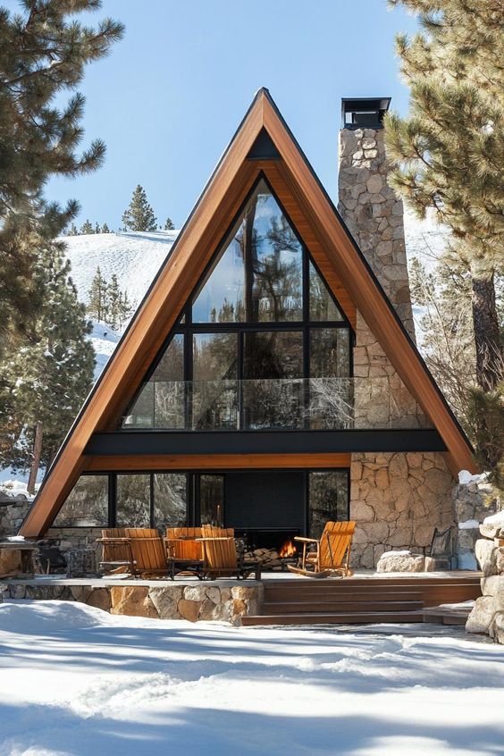 A-frame cabin nestled in snowy woods with large glass windows, fireplace, and outdoor seating area.