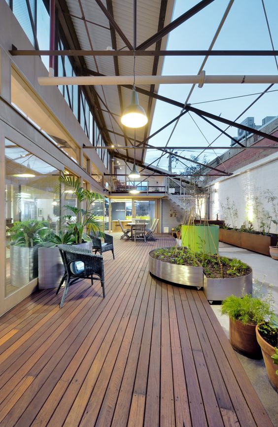 Spacious modern indoor courtyard with wooden flooring, potted plants, seating area, and large windows bringing in ample natural light.