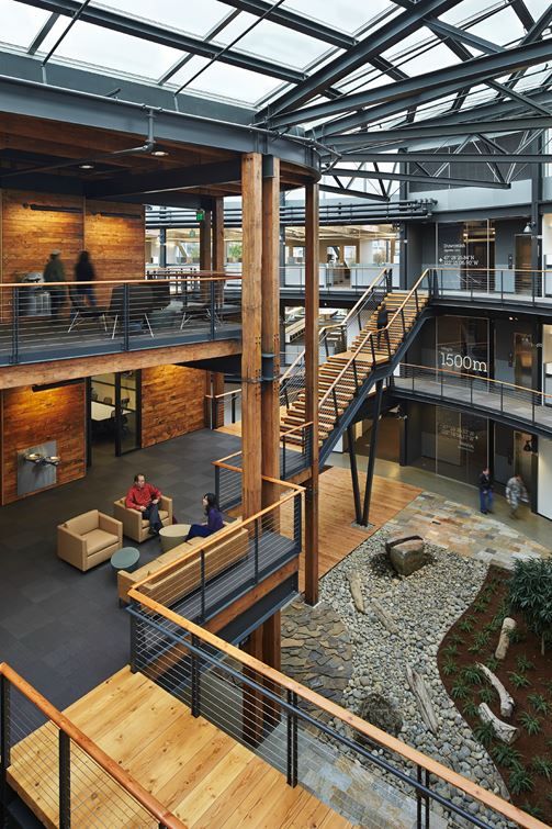 Modern office interior with wooden accents, open staircases, and indoor garden featuring a rock and plant landscape.