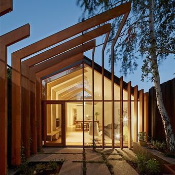 Modern glass house with wooden beams illuminated at night, showcasing contemporary architecture and a stylish, cozy interior.