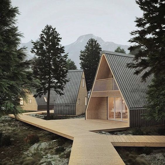 Modern A-frame cabins nestled in a forest with mountain views, connected by wooden walkways. Peaceful and scenic retreat.