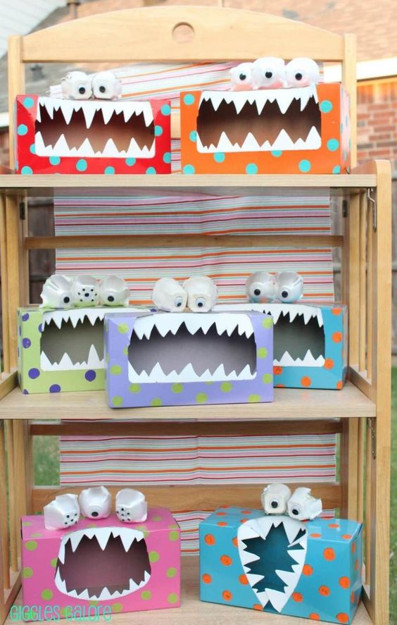 Colorful DIY tissue box monsters with googly eyes and jagged teeth on a wooden shelf, perfect for kids' crafts.