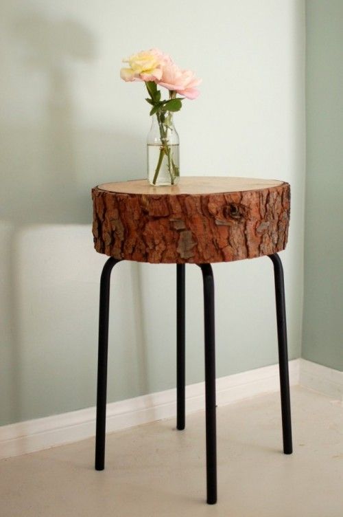 Rustic side table with wooden slab top and black metal legs, decorated with a vase of pink and yellow flowers on a light background.